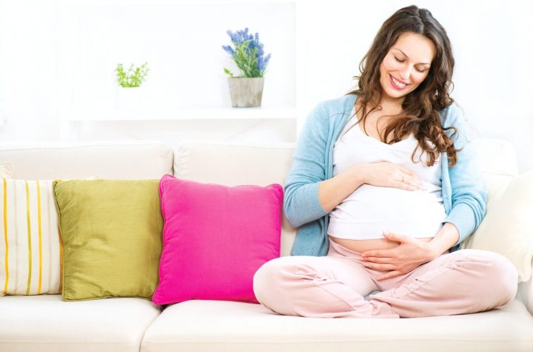 Pregnant woman sitting on a sofa and caressing her belly