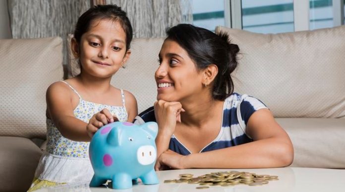 Mother and daughter putting coins into piggy bank - Stock image